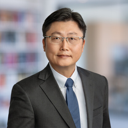 A man wearing glasses, a dark suit, white dress shirt, and blue tie stands in front of a blurred corporate law office, embodying the professionalism of top Chicago lawyers.