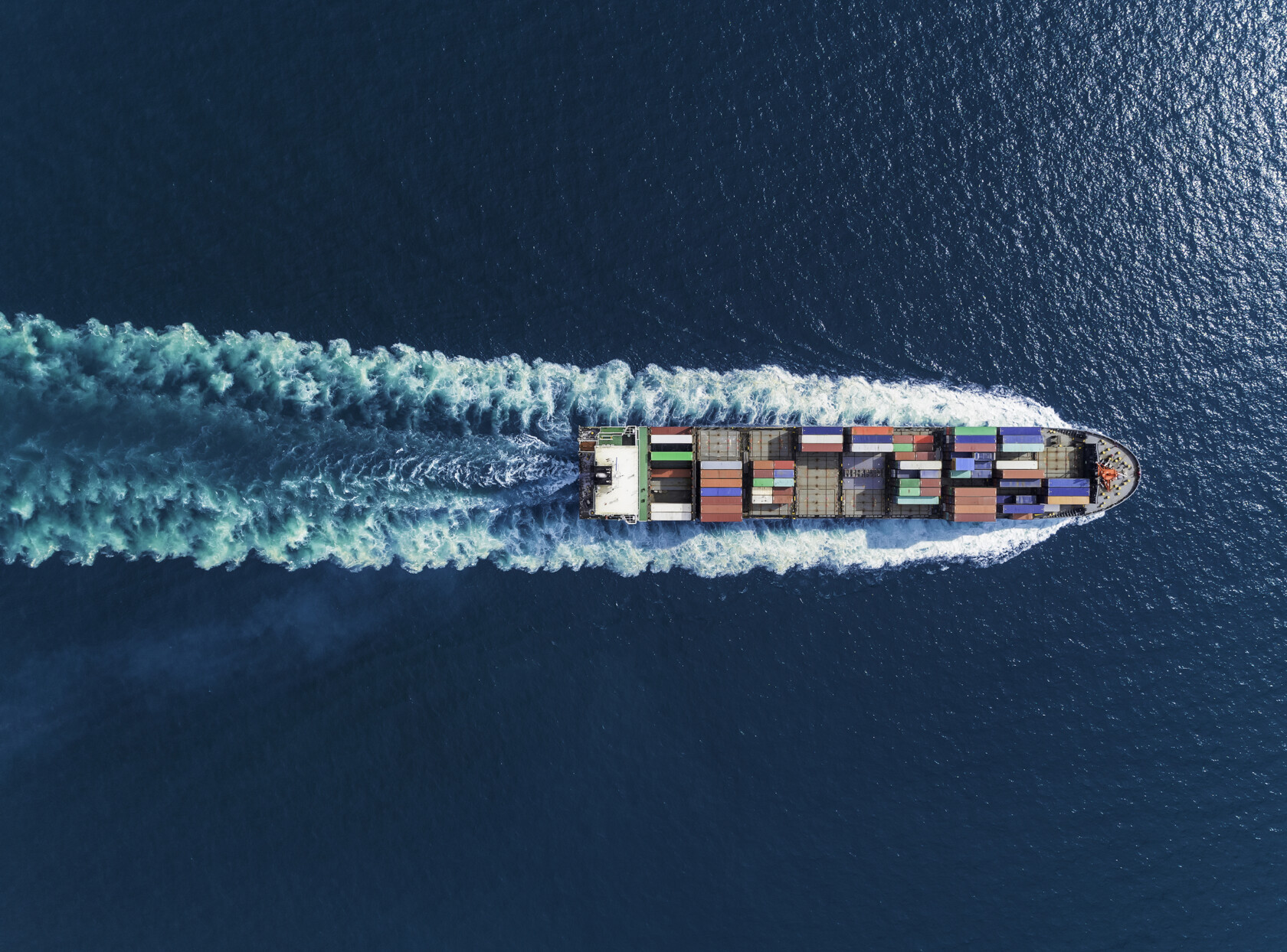 Aerial view of a cargo ship with multicolored containers sailing in blue ocean water, leaving a visible wake—much like how lawyers in Chicago navigate complex cases with precision and expertise.