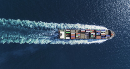 Aerial view of a cargo ship with multicolored containers sailing in blue ocean water, leaving a visible wake—much like how lawyers in Chicago navigate complex cases with precision and expertise.