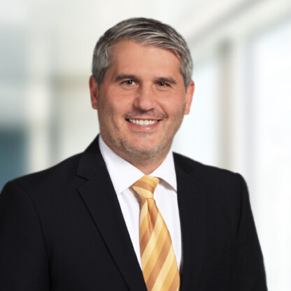 A man in a dark suit, white shirt, and yellow striped tie smiles at the camera in a bright, blurred office setting, embodying the professionalism of top Chicago lawyers.