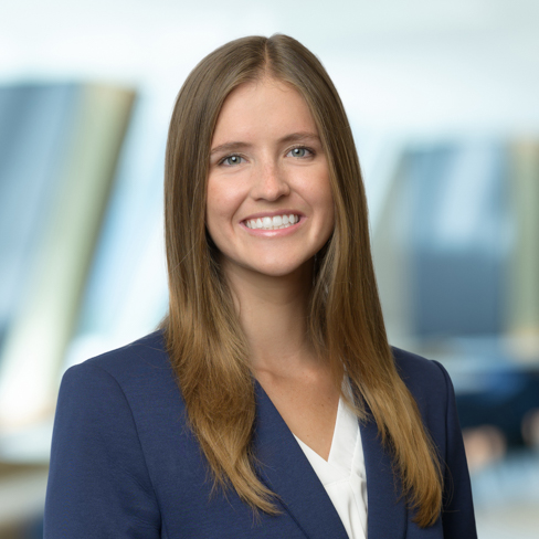 A woman with long straight hair wearing a dark blue blazer and white blouse, smiling, stands in front of a blurred corporate law office background, reflecting the professionalism of top Chicago lawyers.