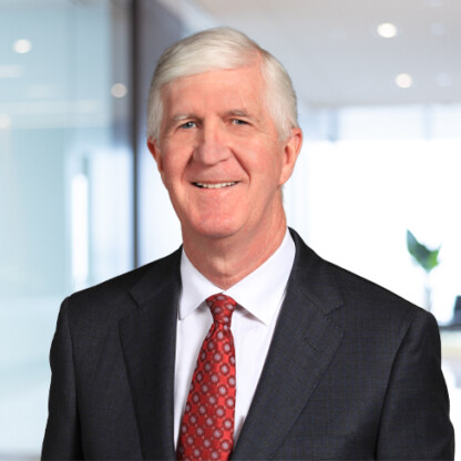 An older man with white hair in a dark suit and red patterned tie stands smiling in a modern corporate law office, reflecting the professionalism of leading lawyers in Chicago.