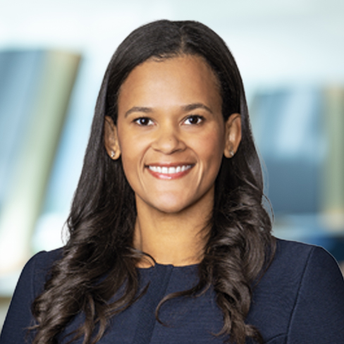 A woman with long, dark hair and a navy blue top smiles at the camera against a blurred law offices background.