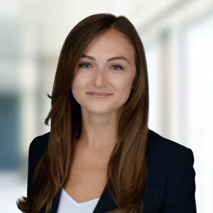 A woman with long brown hair wearing a dark blazer and white top, posing against a blurred indoor background—perfect for representing law offices or offering litigation support.