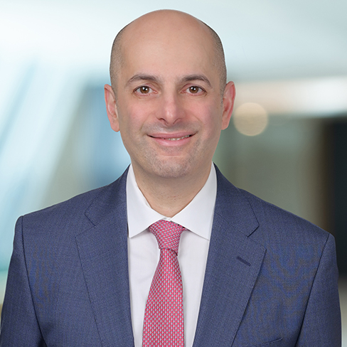 A bald man wearing a blue suit, white shirt, and pink tie is smiling at the camera in a blurred corporate law office, reflecting the professionalism of top Chicago lawyers.