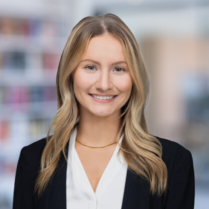 A woman with long blonde hair, wearing a black blazer and white blouse, smiles at the camera in an office setting with blurred bookshelves—representing chicago lawyers specializing in intellectual property law.