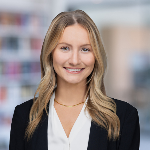 A woman with long blonde hair, wearing a black blazer and white blouse, smiles at the camera in an office setting with blurred bookshelves—representing chicago lawyers specializing in intellectual property law.