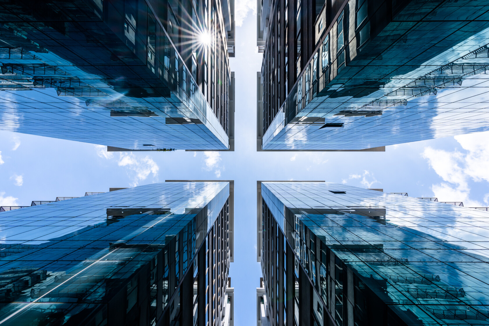 View looking up between four modern glass-clad skyscrapers, with reflections of the sky and sun—an impressive backdrop befitting top Chicago lawyers or a leading corporate law office.
