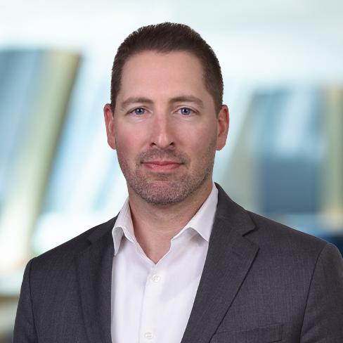 A man in a gray suit jacket and white shirt stands in front of a blurred office background, looking at the camera with a neutral expression, evoking the professionalism seen in top Chicago lawyers and corporate law offices.