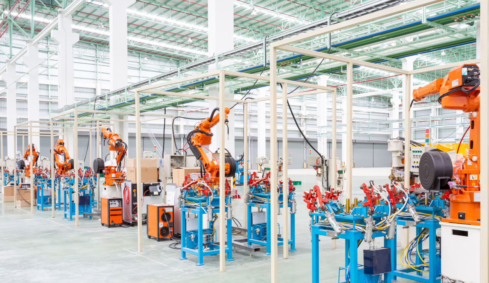 A row of industrial robotic arms assembles products in a modern, automated factory with high ceilings and bright lighting—technology that often requires protection through intellectual property law.