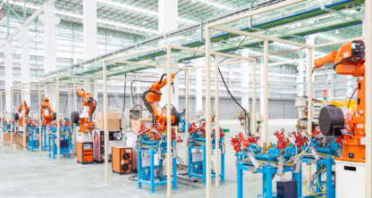 A row of industrial robotic arms assembles products in a modern, automated factory with high ceilings and bright lighting—technology that often requires protection through intellectual property law.