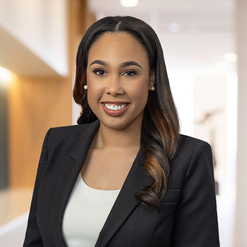 A woman in professional attire smiles at the camera while standing in a modern, well-lit office hallway, representing experienced Chicago lawyers dedicated to excellence.