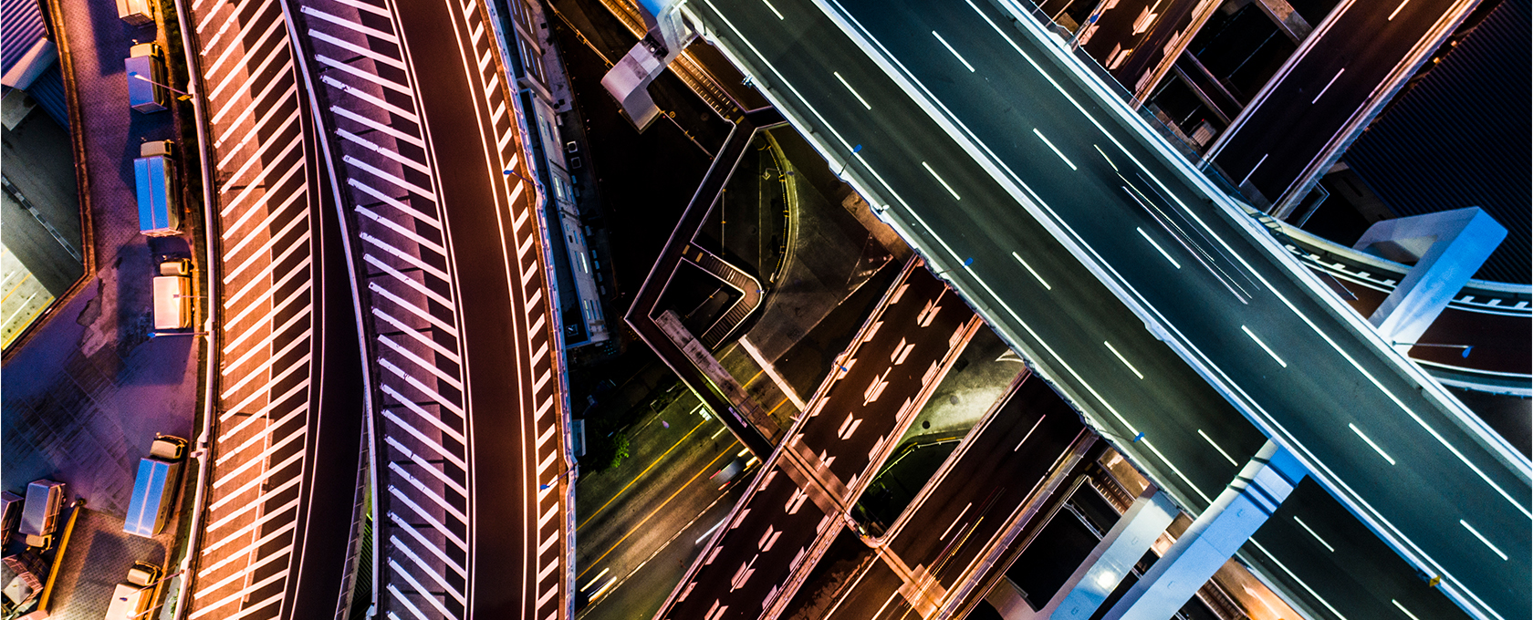 Aerial view of intersecting highways and ramps at night, with marked lanes, streetlights, vehicles on the roads, and the city skyline hinting at the bustling offices of Chicago lawyers nearby.
