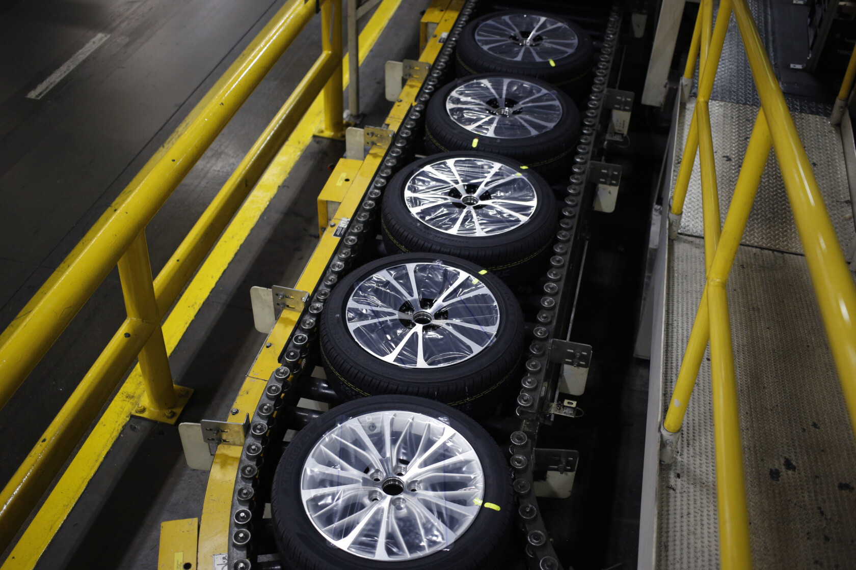 Car wheels with tires are lined up on a conveyor belt in a factory, surrounded by yellow safety railings, similar to the organized precision found in Chicago lawyers’ law offices.