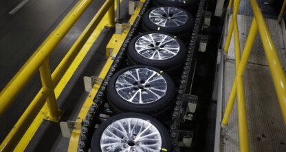 Car wheels with tires are lined up on a conveyor belt in a factory, surrounded by yellow safety railings, similar to the organized precision found in Chicago lawyers’ law offices.