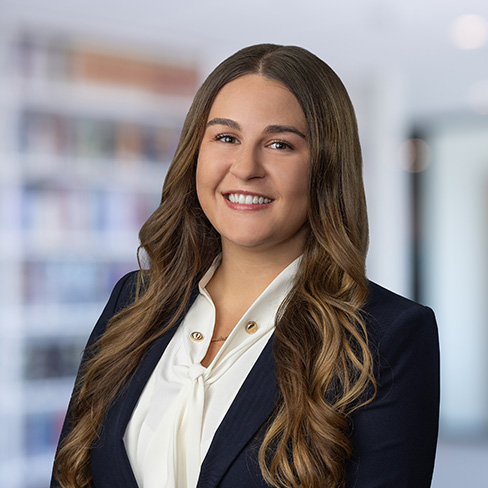 A woman with long brown hair, wearing a black blazer and white blouse, smiles at the camera in a brightly lit, blurred office setting—reflecting the professionalism often seen among leading lawyers in Chicago.