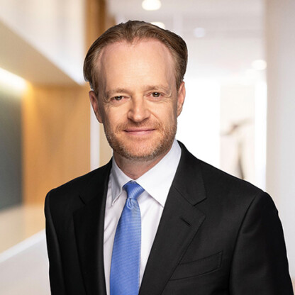 A man in a suit and blue tie stands in a brightly lit office hallway, smiling slightly at the camera—reflecting the professionalism of lawyers in Chicago.