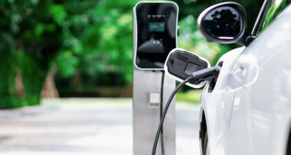 A white electric car is plugged into a charging station outdoors, with trees and a blurred background—perfect for lawyers in Chicago who value innovation and sustainability.