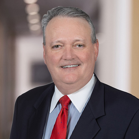 A middle-aged man in a suit and red tie smiles at the camera, standing in a softly blurred indoor setting—an approachable face among experienced Chicago lawyers.