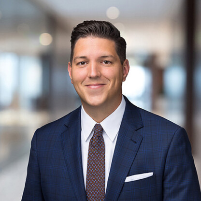 Man in a blue plaid suit, white shirt, and patterned tie stands in a modern, blurred office hallway—smiling at the camera, representing litigation support for law offices.