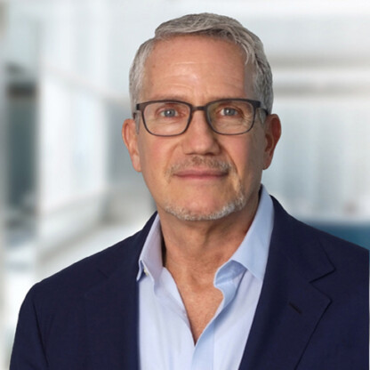 A middle-aged man with gray hair, glasses, and a trimmed beard wearing a navy blazer and light blue shirt stands in a brightly lit office, embodying the professionalism of top lawyers in Chicago.