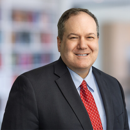 A man in a suit and red tie smiles at the camera with a blurred corporate law office background behind him, reflecting the professionalism of Chicago lawyers specializing in litigation support.