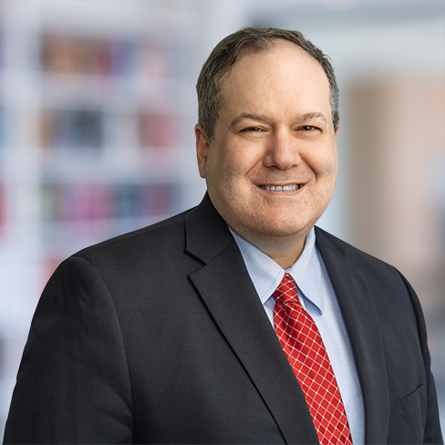 A man in a suit and red tie smiles at the camera with a blurred corporate law office background behind him, reflecting the professionalism of Chicago lawyers specializing in litigation support.