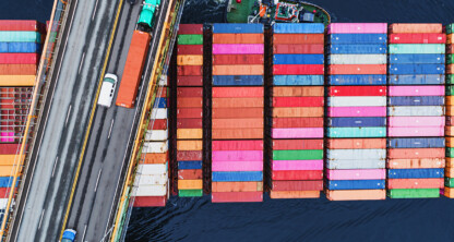 Aerial view of colorful shipping containers stacked on a cargo ship beside a bridge with vehicles over dark water, capturing the dynamic energy of Chicago—home to top corporate law offices and leading lawyers in Chicago.