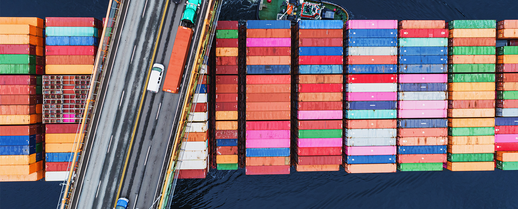 Aerial view of colorful shipping containers stacked on a cargo ship beside a bridge with vehicles over dark water, capturing the dynamic energy of Chicago—home to top corporate law offices and leading lawyers in Chicago.