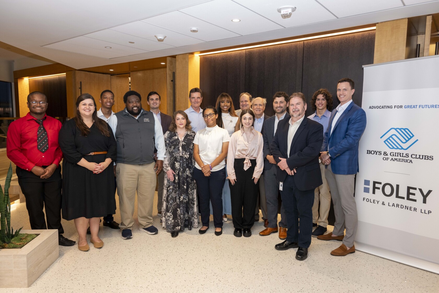 A group of people pose indoors next to a Boys & Girls Clubs of America and Foley & Lardner LLP banner at a corporate law office.