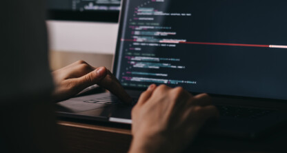 Person typing on a laptop displaying lines of code on a dark-themed screen in a dimly lit law office, highlighting the intersection of technology and intellectual property law.