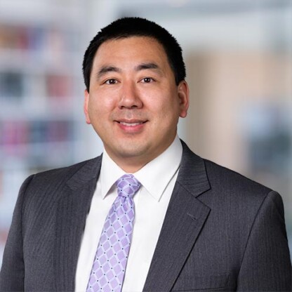 A man in a business suit and patterned tie stands in front of a blurred office background, facing the camera and smiling—representing the professionalism of lawyers in Chicago.