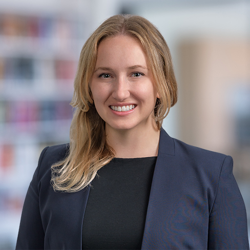 A woman with long blonde hair, wearing a navy blazer and black top, smiles at the camera in a blurred office setting, representing Chicago lawyers specializing in intellectual property law.