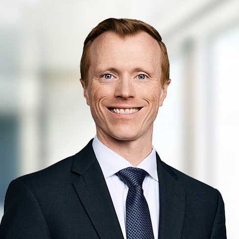A man in a suit and tie smiles at the camera in a brightly lit, modern corporate law office.