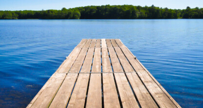 A wooden dock extends over a calm blue lake with a tree-lined shore visible in the distance under a clear sky—an unexpected retreat for busy Chicago lawyers seeking peace away from the city's litigation support demands.