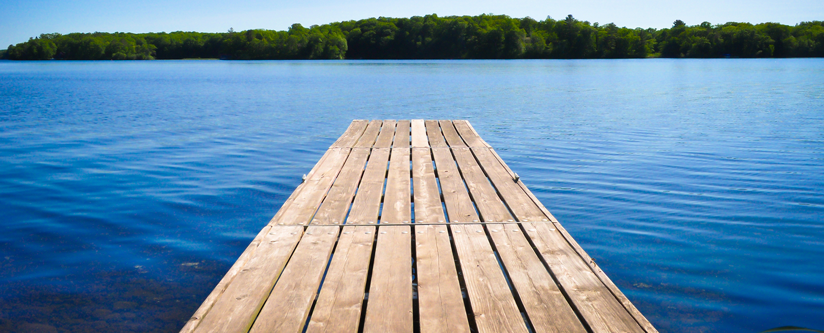A wooden dock extends over a calm blue lake with a tree-lined shore visible in the distance under a clear sky—an unexpected retreat for busy Chicago lawyers seeking peace away from the city's litigation support demands.