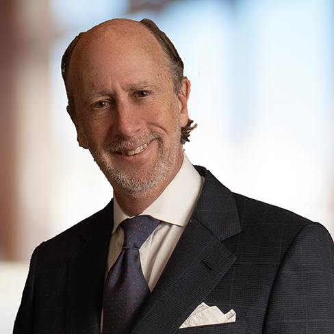 A middle-aged man with thinning hair and a beard, wearing a dark suit, white shirt, and patterned tie, stands in front of a blurred background—representing experienced lawyers in Chicago specializing in intellectual property law.