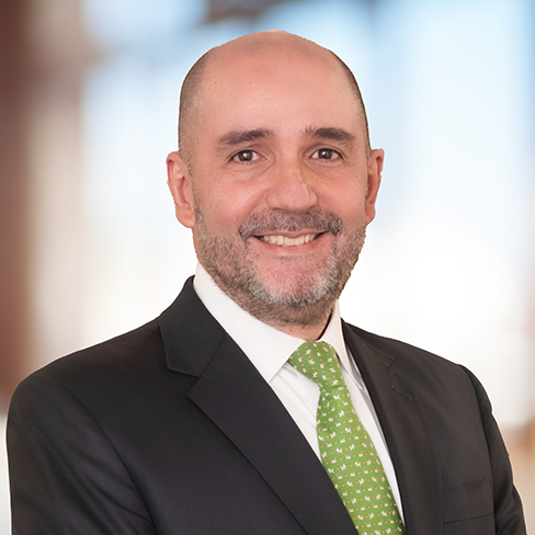 A man in a dark suit, white shirt, and green patterned tie is smiling at the camera with a blurred background, reflecting the professionalism found in top Chicago lawyers and leading corporate law office environments.