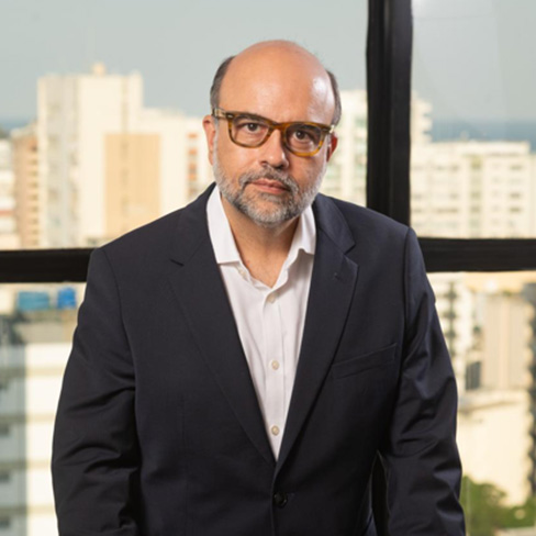A man in a suit and glasses stands indoors in front of a window with a cityscape, representing Chicago lawyers who specialize in intellectual property law.