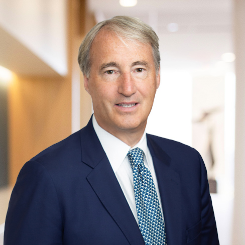A middle-aged man in a blue suit and patterned tie stands in a brightly lit corporate law office hallway, looking at the camera—representing the professionalism of Chicago lawyers.