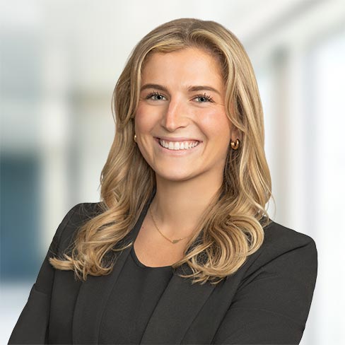 A woman with long blonde hair, wearing a black blazer and top, smiles at the camera in a brightly lit office setting, reflecting the professionalism of lawyers in Chicago specializing in litigation support.