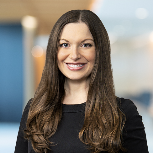 Woman with long brown hair wearing a black top, smiling and standing in a brightly lit corporate law office in Chicago.