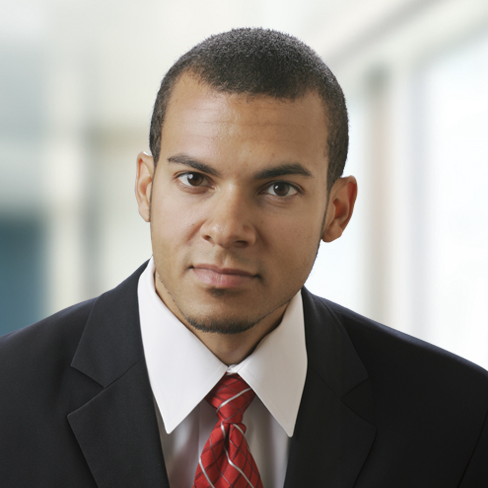 A man in a dark suit, white shirt, and red tie looks at the camera with a neutral expression; blurred office background—a professional image suitable for chicago lawyers or those offering litigation support.