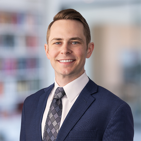 A man in a navy blue suit, white shirt, and patterned tie smiles at the camera in a blurred law offices setting, reflecting the professionalism of lawyers in Chicago.
