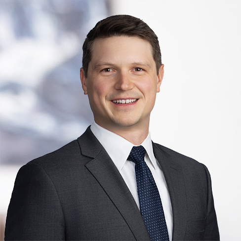 A man in a dark suit, white shirt, and navy tie stands smiling against a blurred light background, embodying the professionalism found in top corporate law offices.