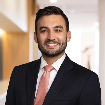A man in a dark suit and pink tie smiles at the camera while standing in a brightly lit office hallway, reflecting the professionalism of leading lawyers in Chicago specializing in intellectual property law.