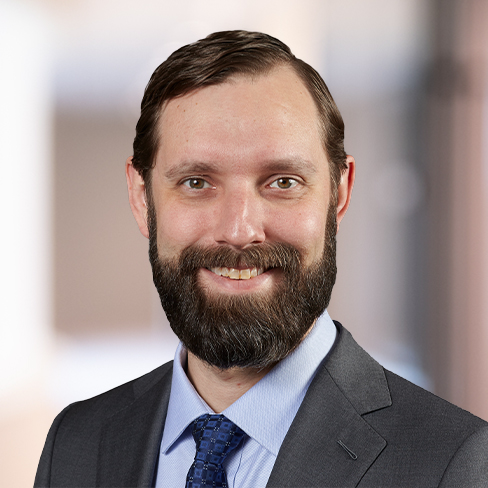 A man in a suit and tie with a beard and short hair smiles at the camera, embodying the professionalism of Chicago lawyers. The background is softly blurred.