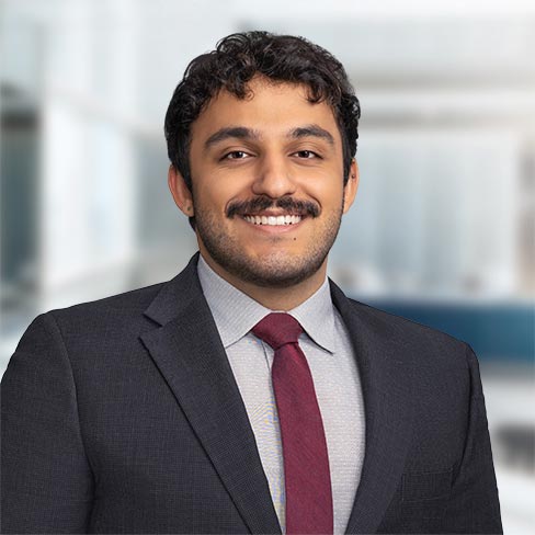 A man with curly hair and a mustache, wearing a dark suit, light shirt, and red tie, smiles at the camera in an office setting, embodying the professionalism of top lawyers in Chicago.