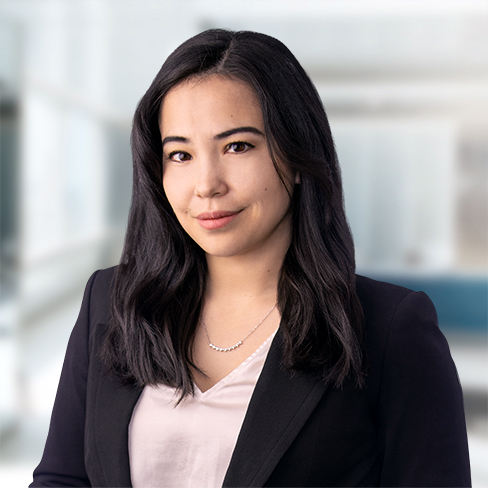Woman with long dark hair wearing a black blazer over a light blouse, standing in a modern, blurred office setting—reflecting the professionalism of top Chicago lawyers and their commitment to providing exceptional litigation support.