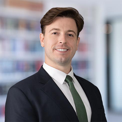 A man in a suit and green tie smiles at the camera in a professional indoor setting, with blurred bookshelves hinting at a corporate law office for Chicago lawyers in the background.